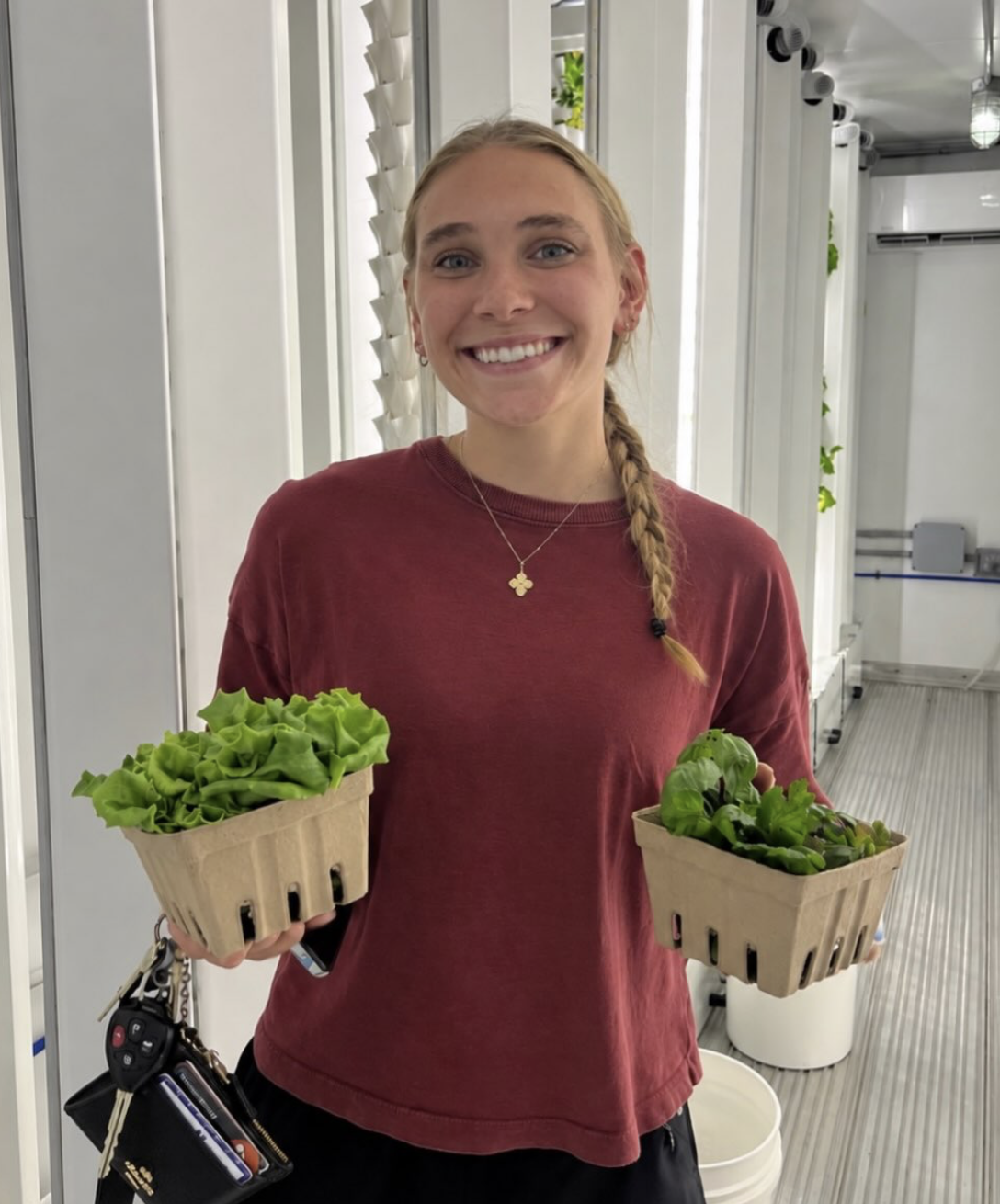 Student holding baskets of fresh lettuce and herbs in the growing corridor