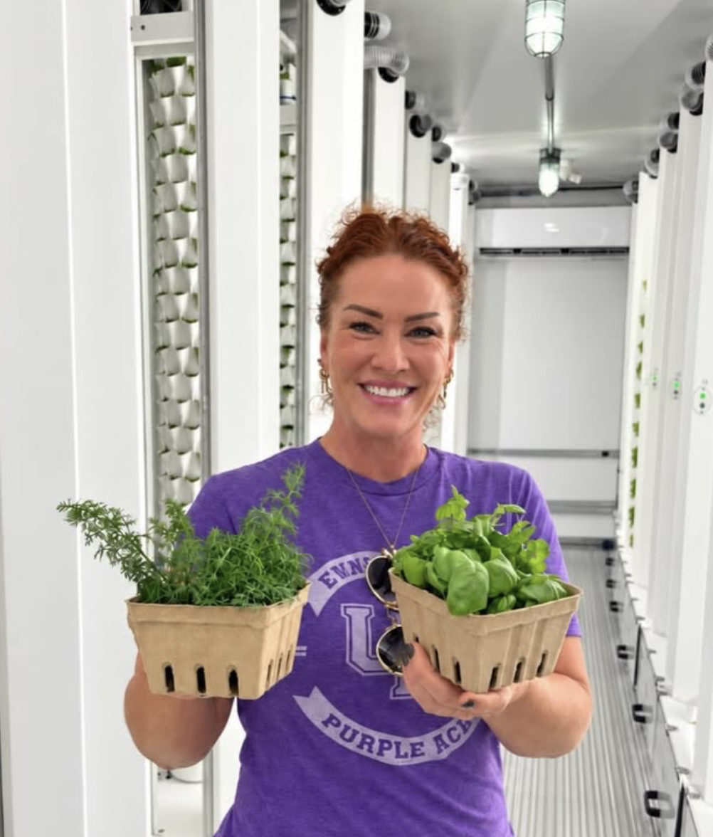 Student holding baskets of fresh basil and dill between hydroponic towers