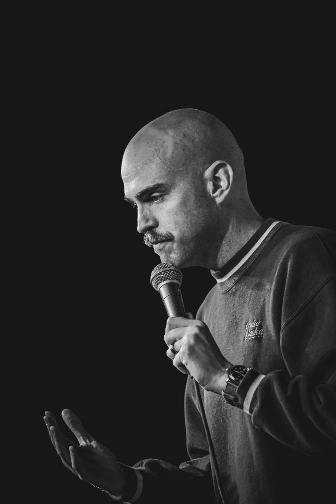 Black-and-white portrait of Scott Bedgood performing stand-up, mic in hand