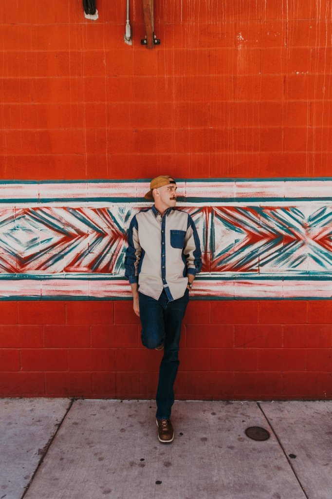 Scott Bedgood leaning against a vibrant red brick wall with a geometric mural