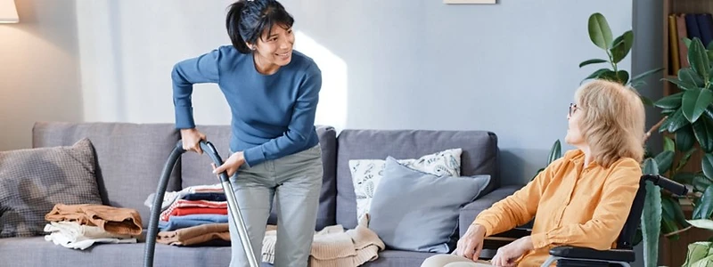A Mobilize Cleaning caregiver vacuuming while a senior sits in a wheelchair nearby