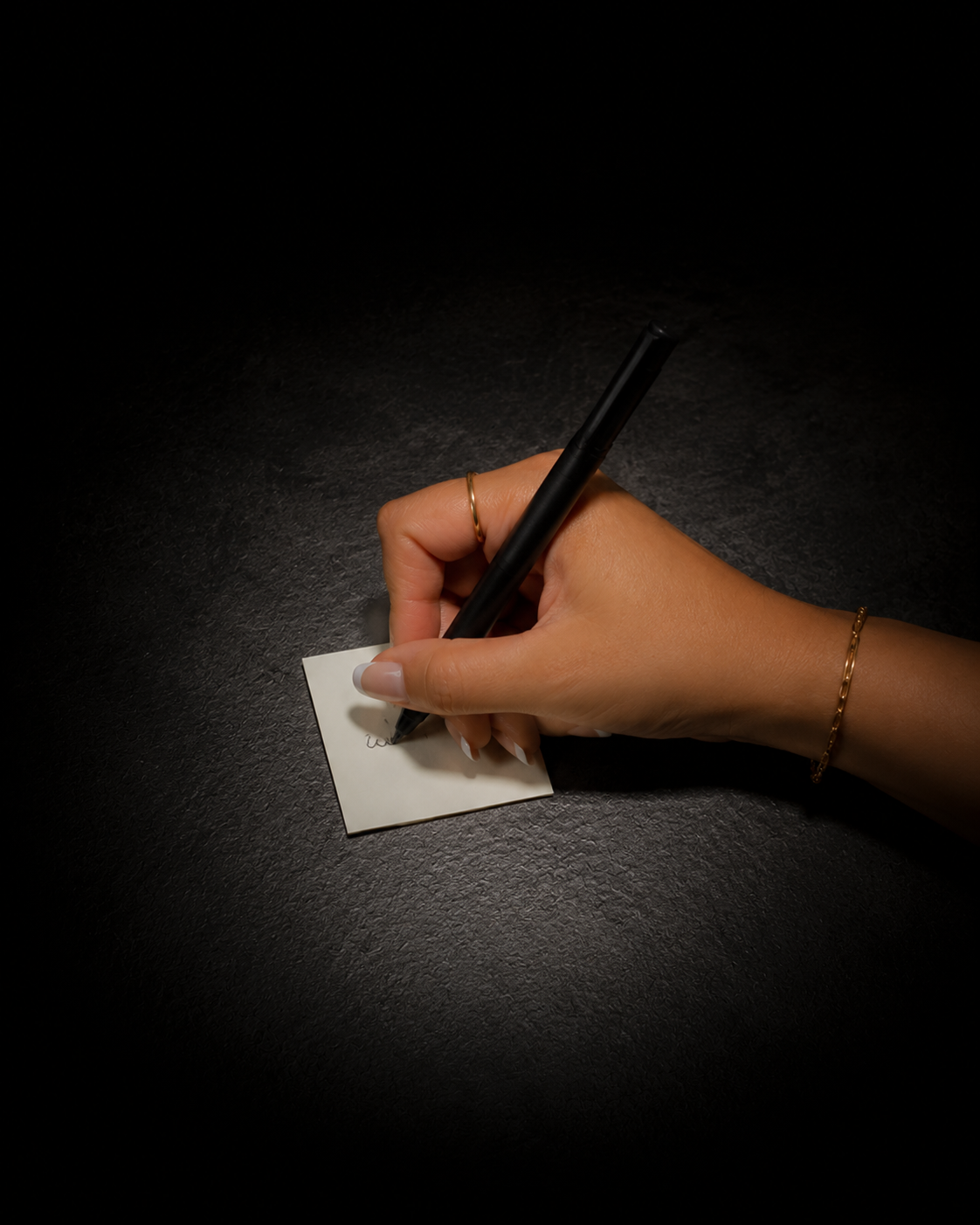 A hand writing on a small white piece of paper under a focused spotlight.