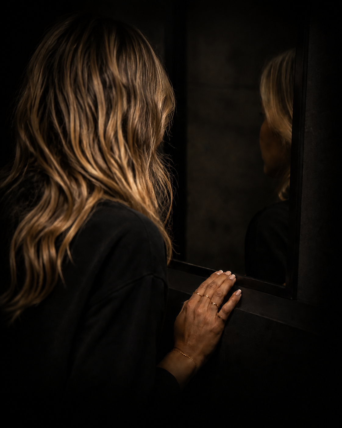 A woman reflecting as her hand touches a dark mirror.