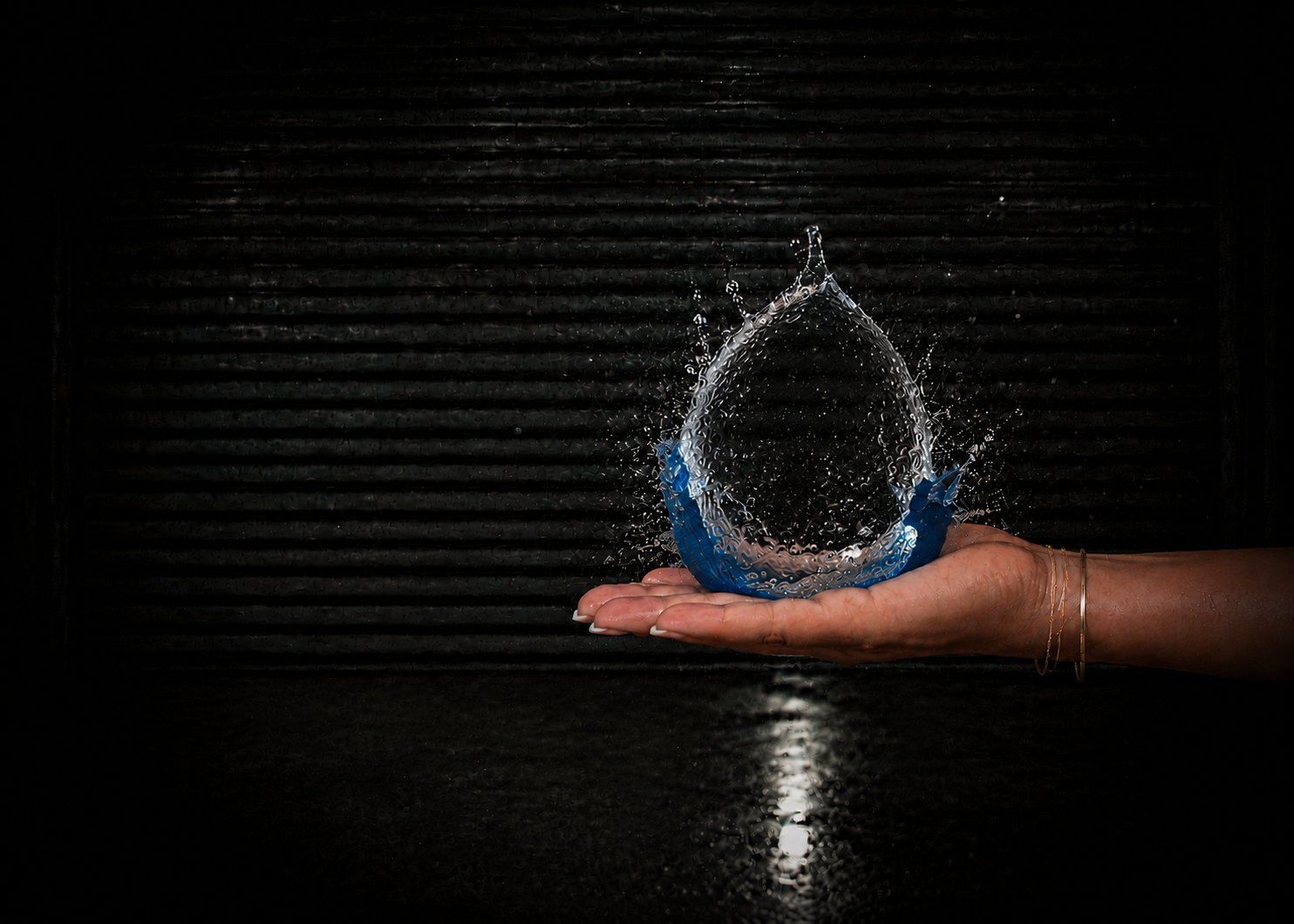 A hand holding a glowing water droplet in a dark cinematic setting