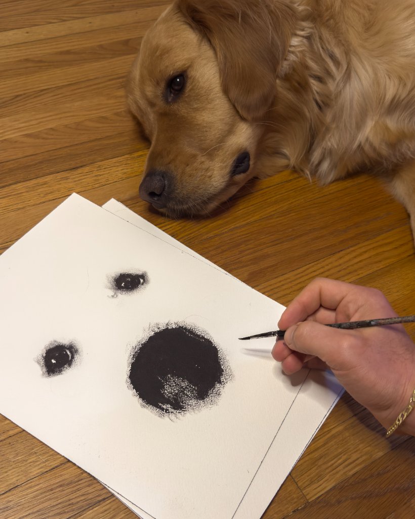 A golden retriever watching a hand-drawn portrait in progress on a wooden floor