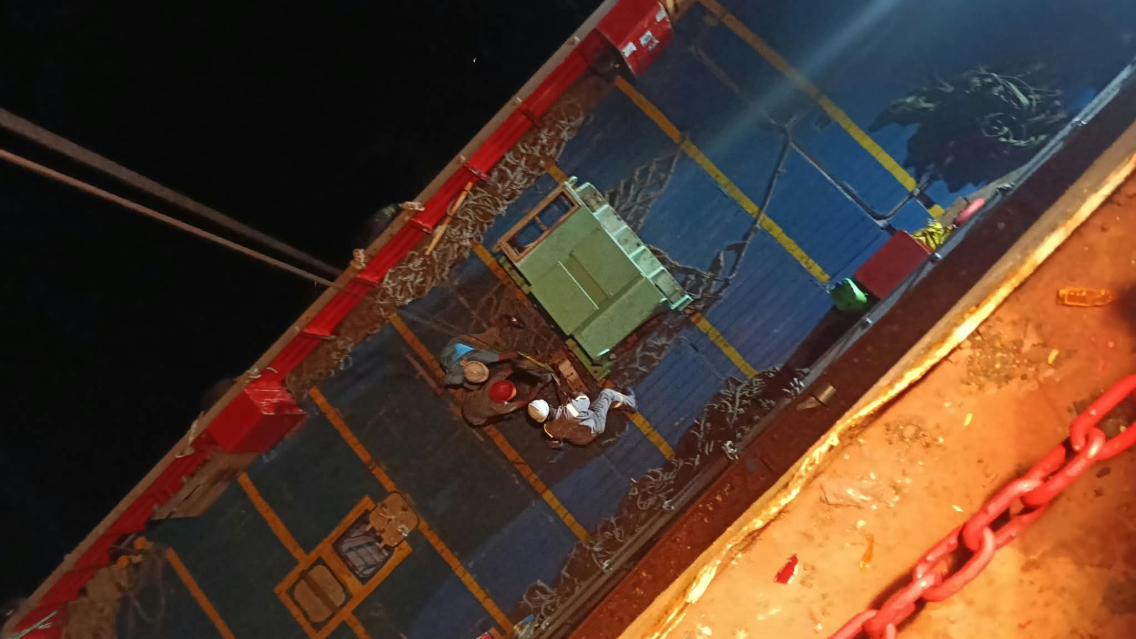 Overhead view of crew guiding a heavy-lift machinery component on the vessel deck at night