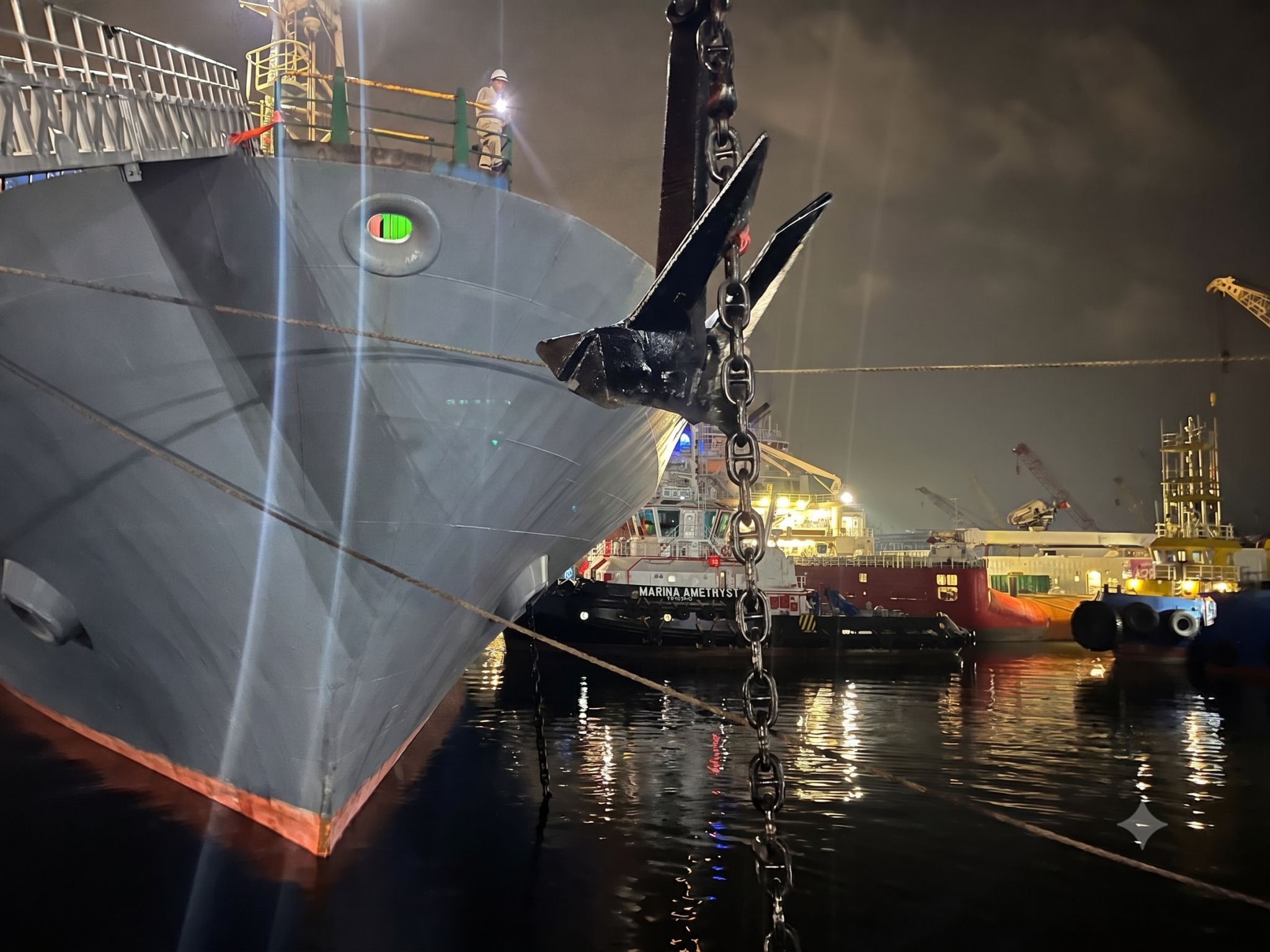 Replacement anchor being hoisted beside the bow of the container vessel with tug support alongside