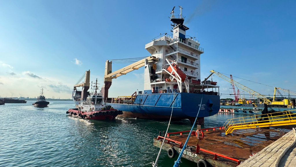 Heavy-lift cargo vessel with tug alongside in Singapore harbour