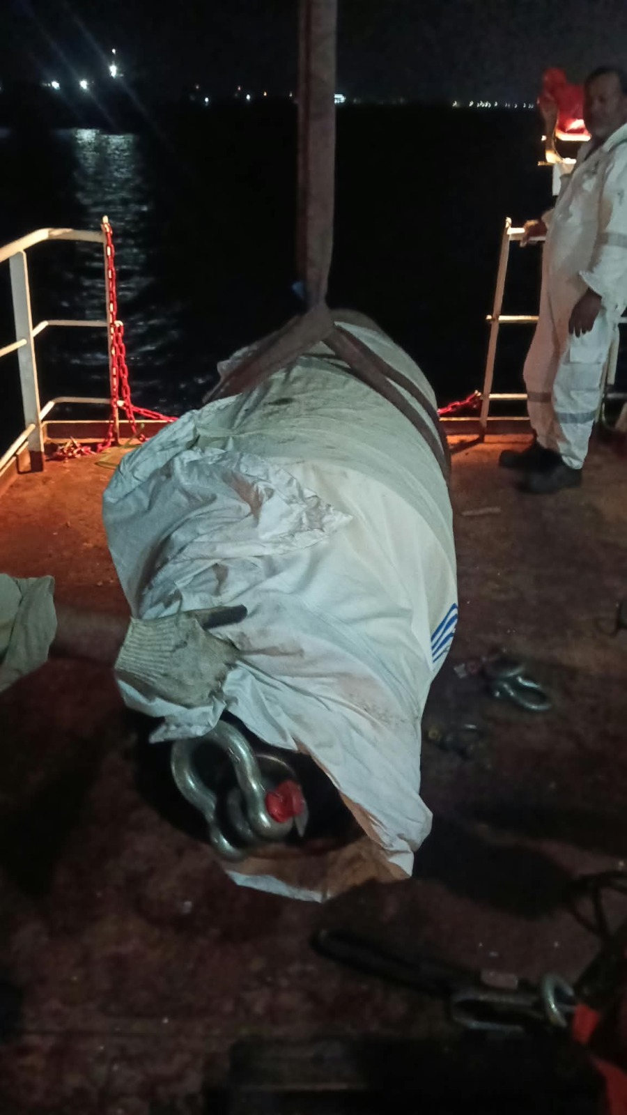 Wrapped cylindrical component lifted by crane with a crew member in coveralls overseeing the operation
