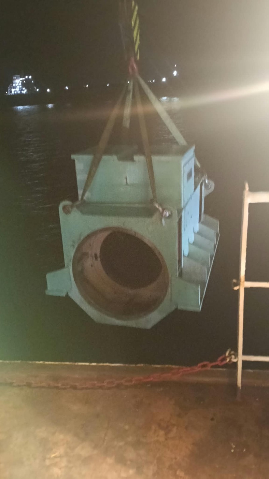Heavy machinery housing suspended by crane hook during night lifting operations at anchorage
