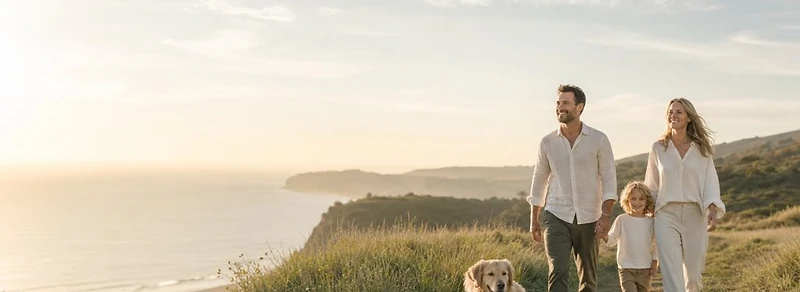 Famiglia con cane che cammina su un sentiero a strapiombo sul mare al tramonto