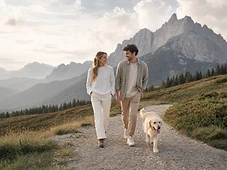 Coppia che passeggia con il cane su un sentiero di montagna al tramonto
