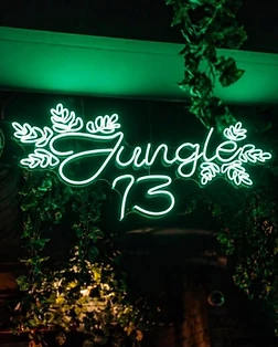 Jungle 13 club interior in Barcelona with green neon sign and hanging plants