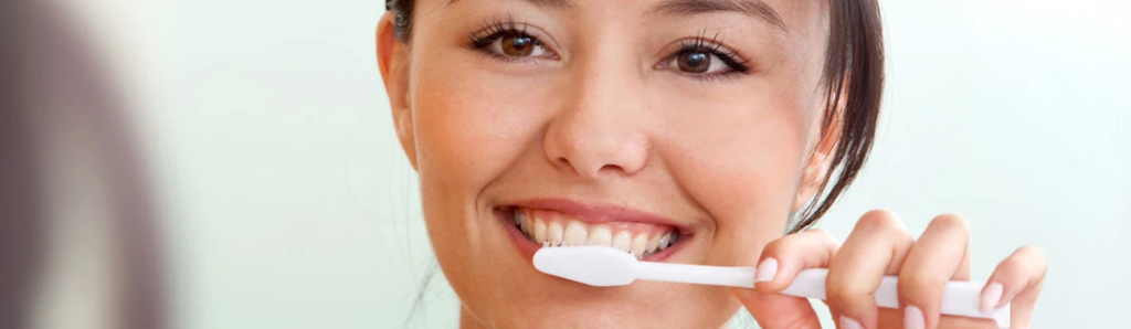 Woman brushing her teeth and smiling — healthy gums at Mega Dental Richmond TX