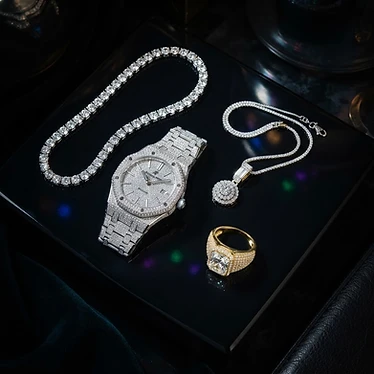 Flat lay of iced out jewelry pieces on obsidian surface