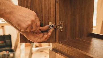 Close-up of custom-built wood cabinetry with a craftsman adjusting a cabinet door hinge