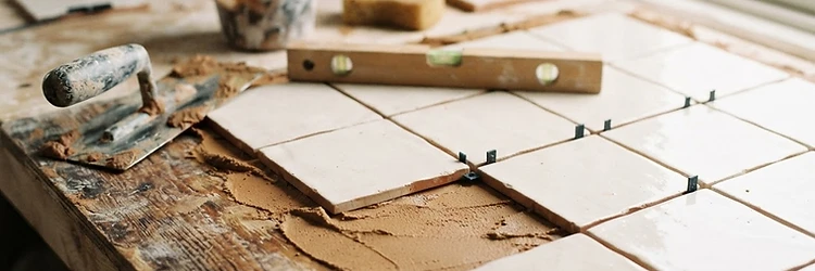 Close-up of careful hand-laid tile work with a trowel and level in natural light