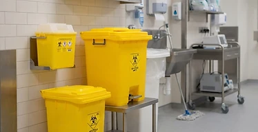 Sharps Container System — Hospital clinical waste area with yellow biohazard bins and sharps containers