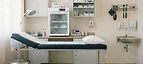 Primary Health Centre - Basic — Rural primary health centre clinic interior with examination couch, vaccine refrigerator and supply cabinets