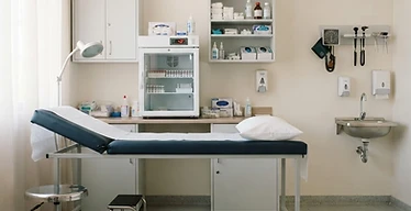 Primary Health Centre - Basic — Rural primary health centre clinic interior with examination couch, vaccine refrigerator and supply cabinets