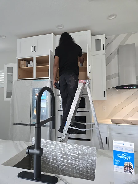 Final post-construction detail cleaning of a new kitchen in a Westlake home built by Mintos Home, with technician cleaning inside upper cabinets and appliances in protective wrap