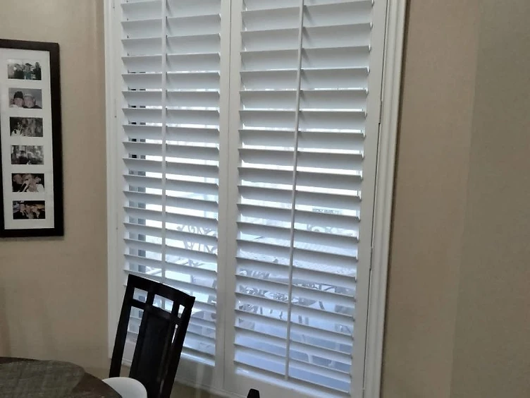 White plantation shutters installed on a double window in a dining room