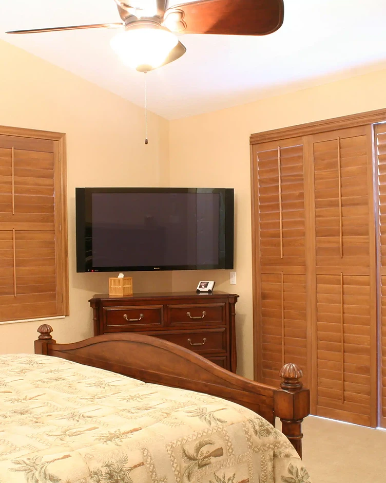 Bedroom with warm wood-toned plantation shutters installed on windows and a sliding door