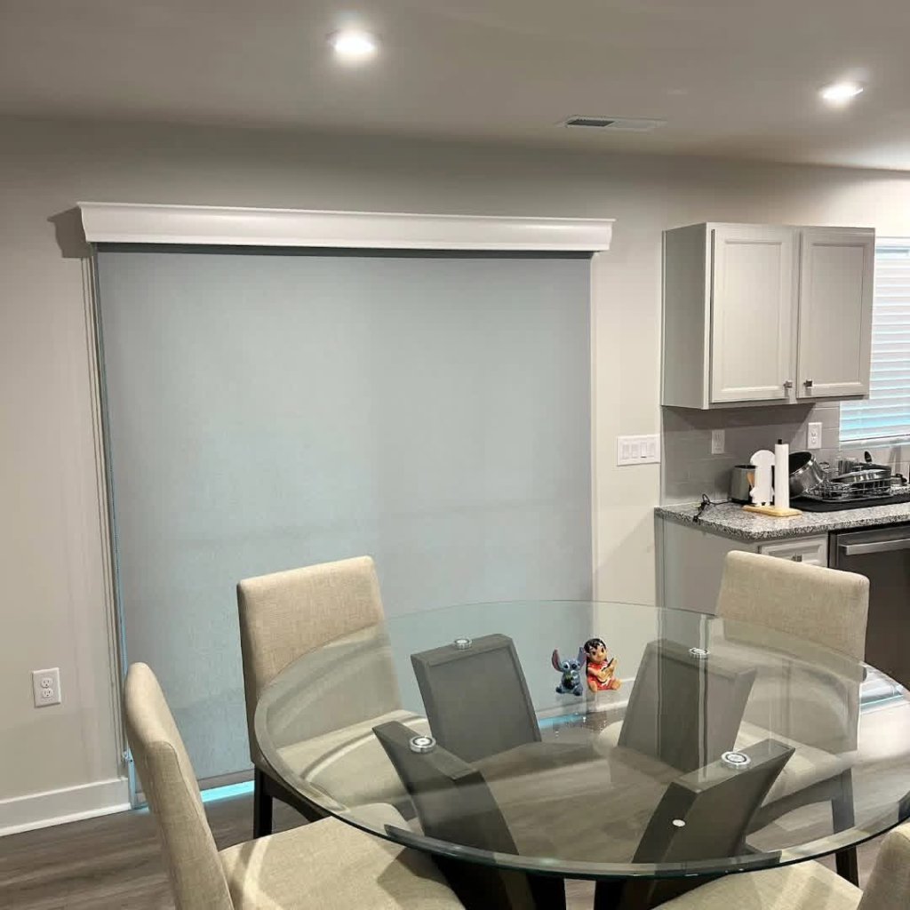 Dining area with custom roller shade and white cornice above a round glass table