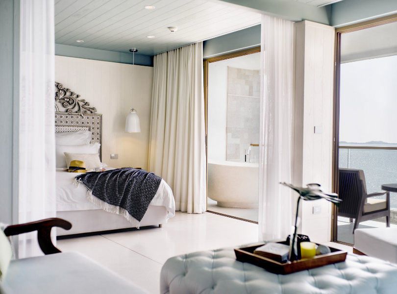 Luxury suite interior with bed, freestanding bathtub and sea-view balcony