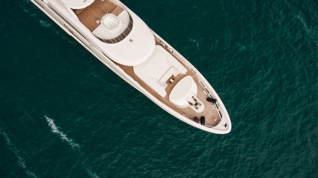 Aerial top-down view of a white superyacht bow cutting through deep teal water