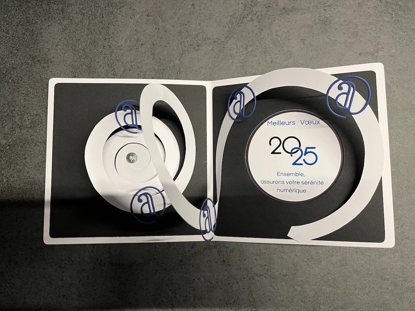 Carte de vœux 2025 artisanale en relief, spirales de papier blanc et monogrammes bleus sur fond noir
