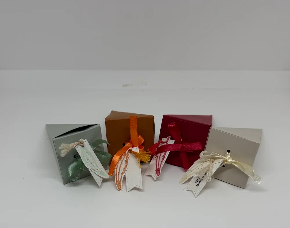 Quatre boîtes cadeaux artisanales colorées ornées de rubans de satin et d'étiquettes plumes faites main