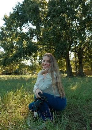 Emma crouching in a grassy field holding her camera