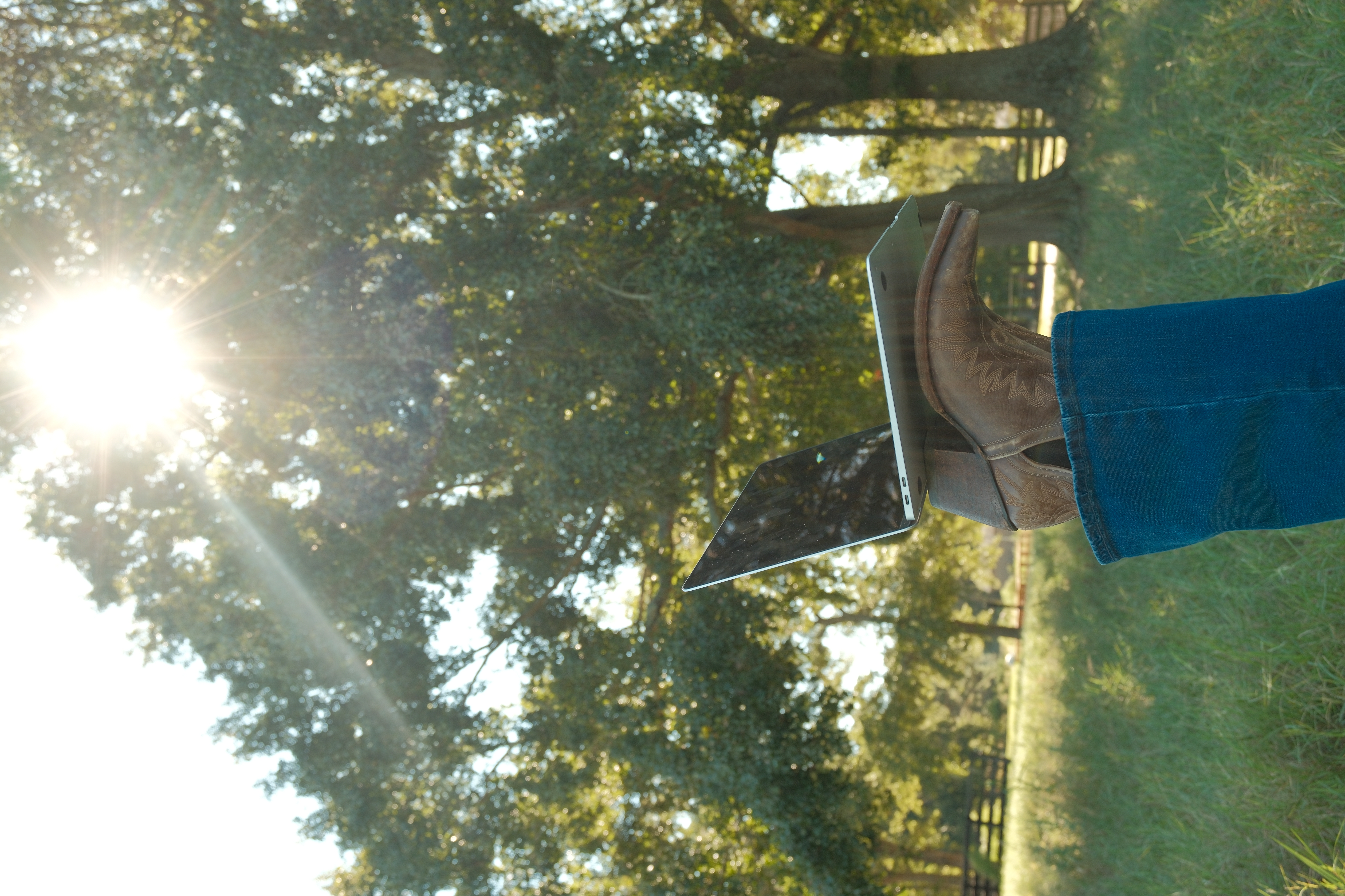 A laptop resting on a cowboy boot in a sunlit field