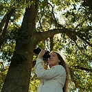 Emma looking through her camera under the trees
