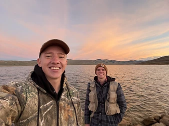 Ben and Aaron, the All Is Bright holiday lighting installers, at a lake at sunset