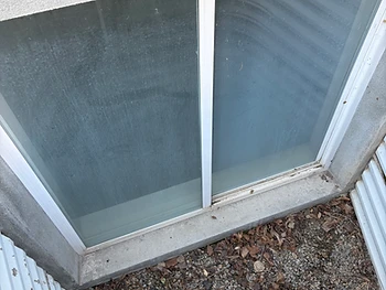 A basement window covered in cloudy hard water mineral haze and grime before cleaning