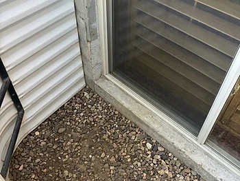 The same window well cleared of debris, with clean gravel showing after cleaning