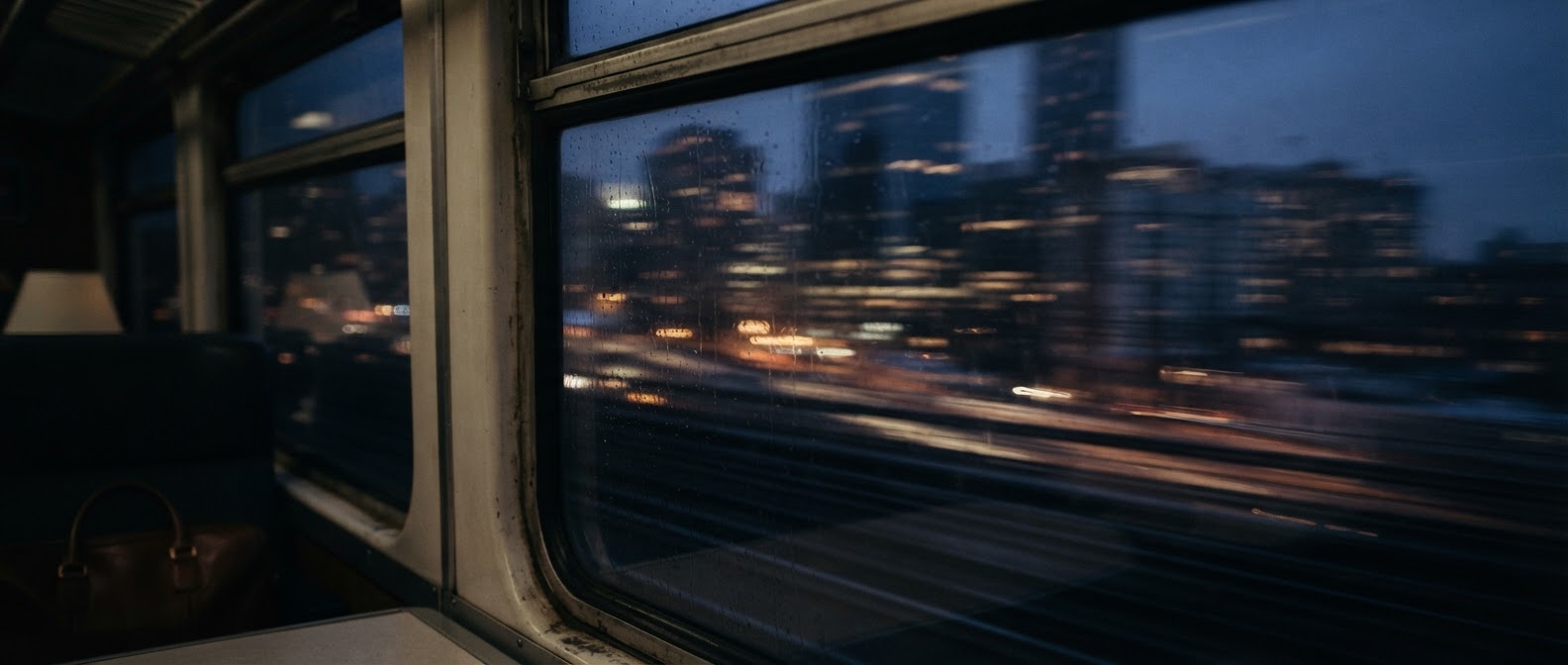 A city blurred past the window of a moving train at blue hour