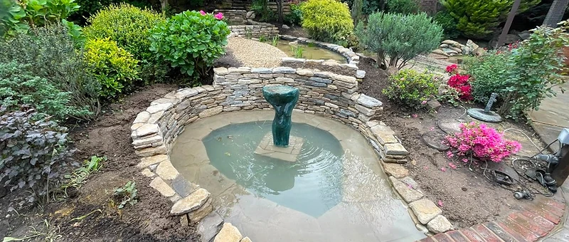 Garden with central stone water feature and established planting in Surrey