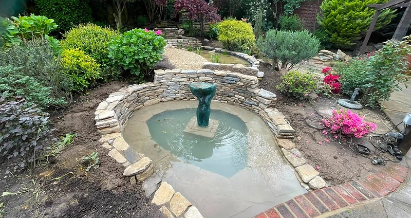 Completed circular pond with drystone walling and stone sculpture in Surrey