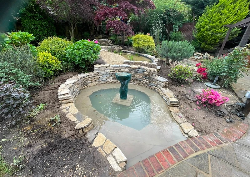 Drystone-walled pond with stone sculpture and established planting, Surrey