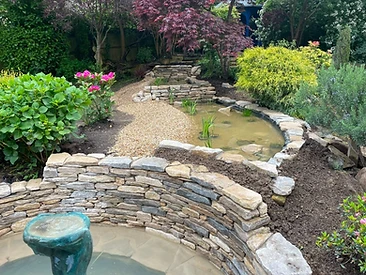 Circular stone pond with drystone walling in a completed Surrey garden
