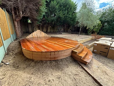 Finished circular timber deck with reddish-brown stain and curved slatted backrest in Surrey