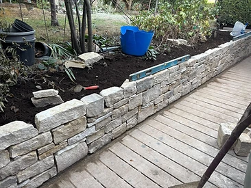 Natural stone retaining wall in a garden with raised soil bed and timber decking in Surrey