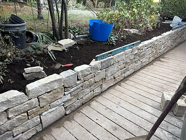 Natural stone retaining wall in a garden with raised soil bed and timber decking in Surrey