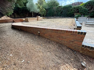 Curved red brick garden retaining wall with dark coping separating patio and planting bed in Surrey