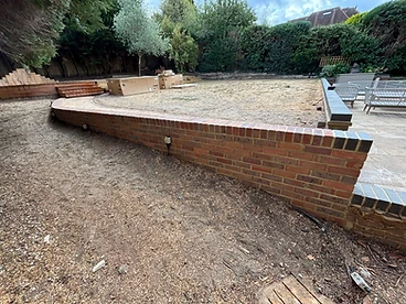 Curved red brick garden retaining wall with dark coping separating patio and planting bed in Surrey