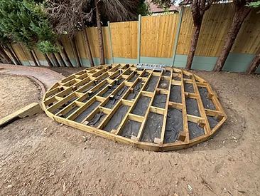 Circular timber deck frame built from pressure-treated joists on landscape fabric in Surrey