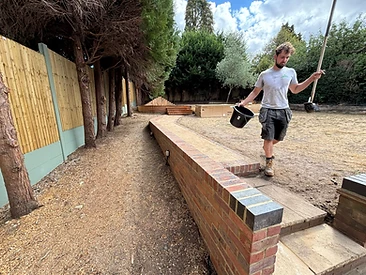 Curved red brick retaining wall with stone coping alongside a sandy construction path in Surrey